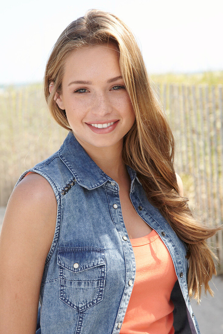 A young blonde woman on a beach wearing an orange top