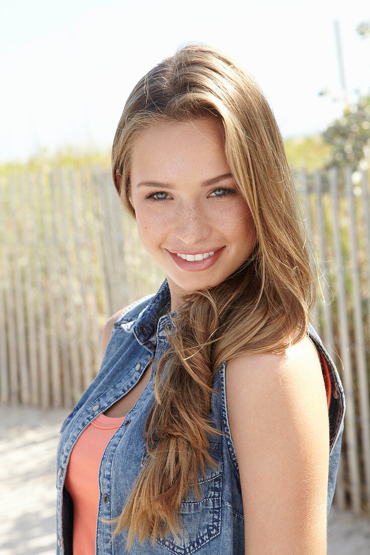 A young blonde woman on a beach wearing an orange top