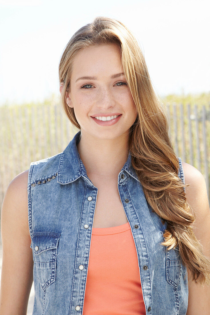 A young blonde woman on a beach wearing an orange top