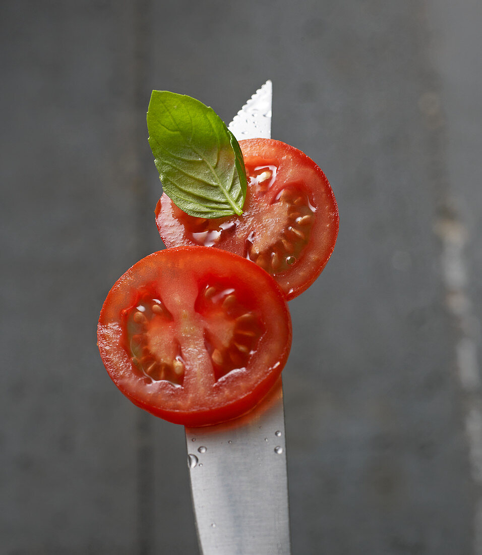 Tomatenscheiben mit Basilikumblatt auf Messerspitze mit Wassertropfen