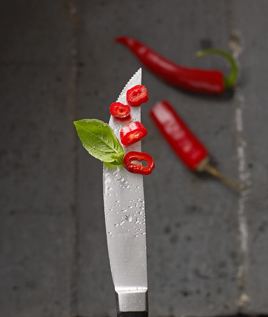 Red chilli rings on a knife tip with water droplets
