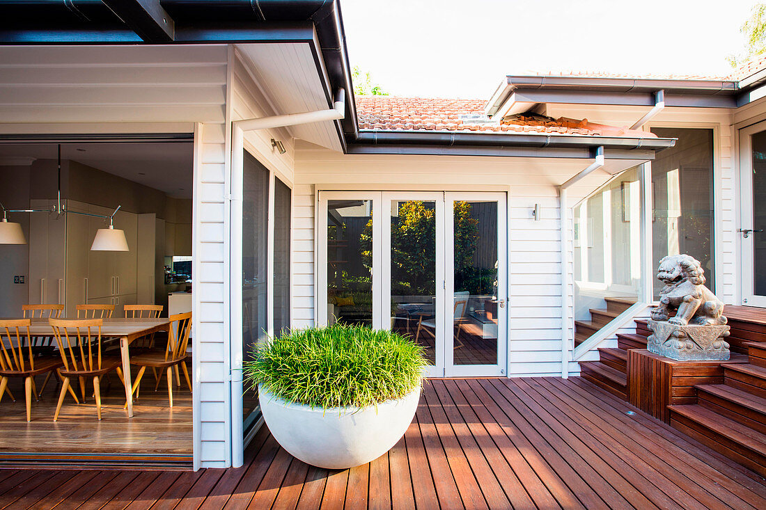 Terrasse mit dunklem Holzboden am Haus mit offener Tür zum Esszimmer