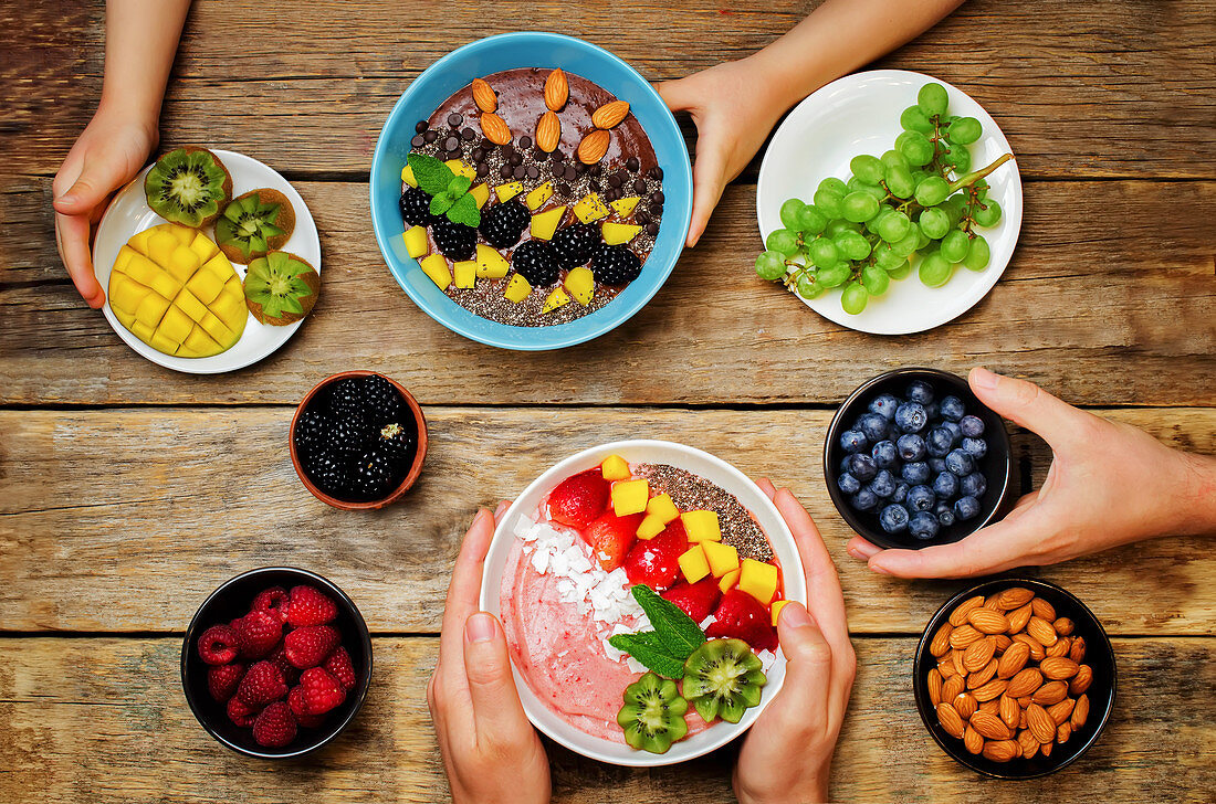 Hände mit gesunden Smoothie Bowls mit Früchten und Beeren