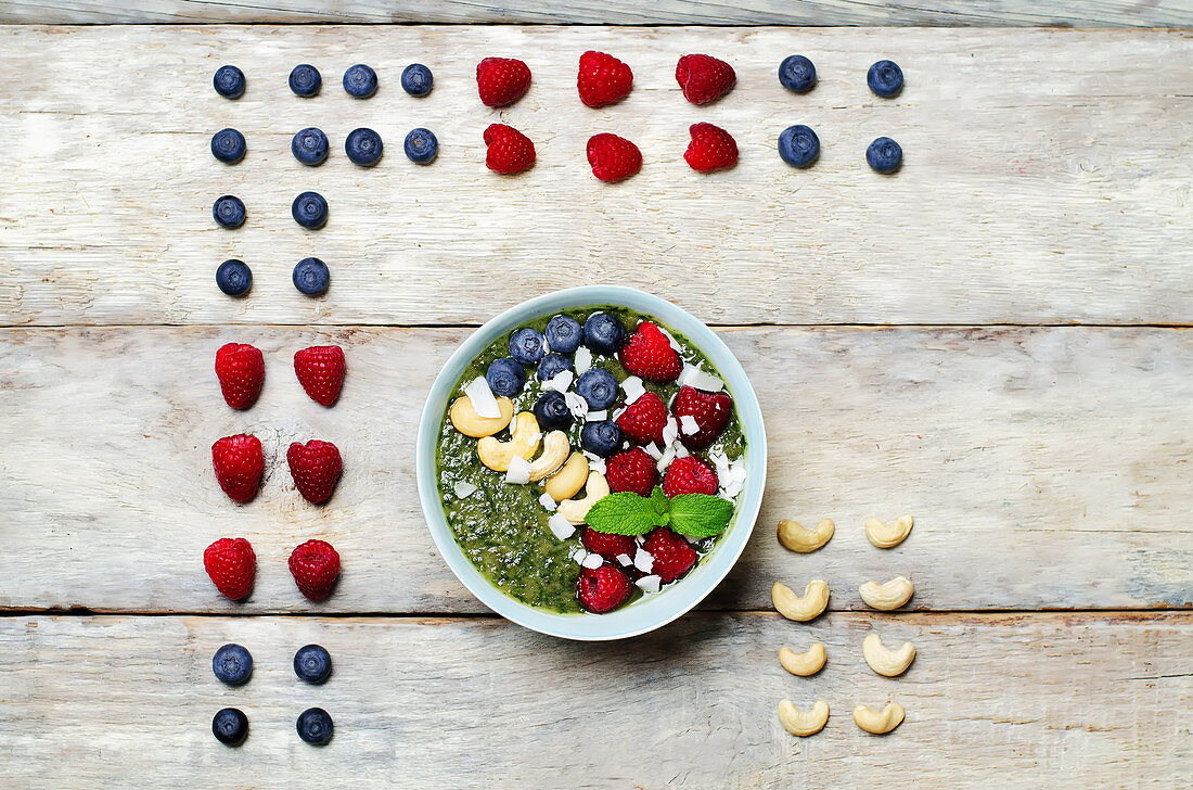 Spinat-Smoothie-Bowl mit Kokosnussflocken, Himbeeren, Blaubeeren und Cashews