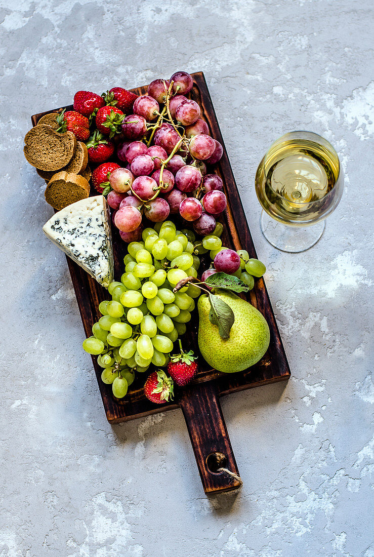 Blauschimmelkäse, Brot, Obst auf Schneidebrett, daneben ein Glas Weißwein