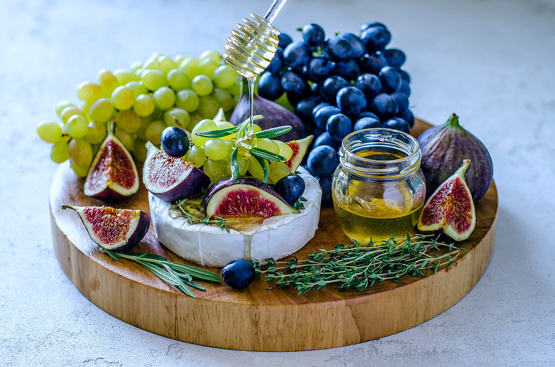 Camembert cheese with figs, honey, grapes and fragrant herbs on a cutting board