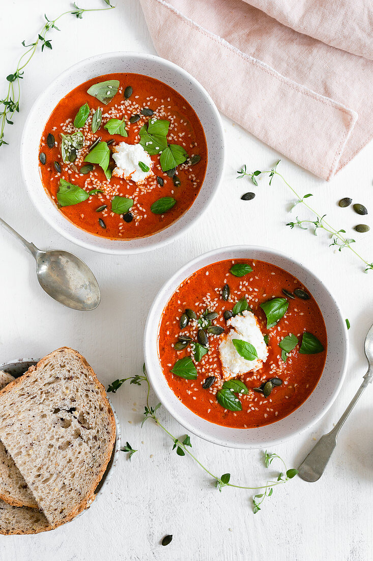 Two bowls of roasted tomato soup topped with fresh basil and ricotta cheese