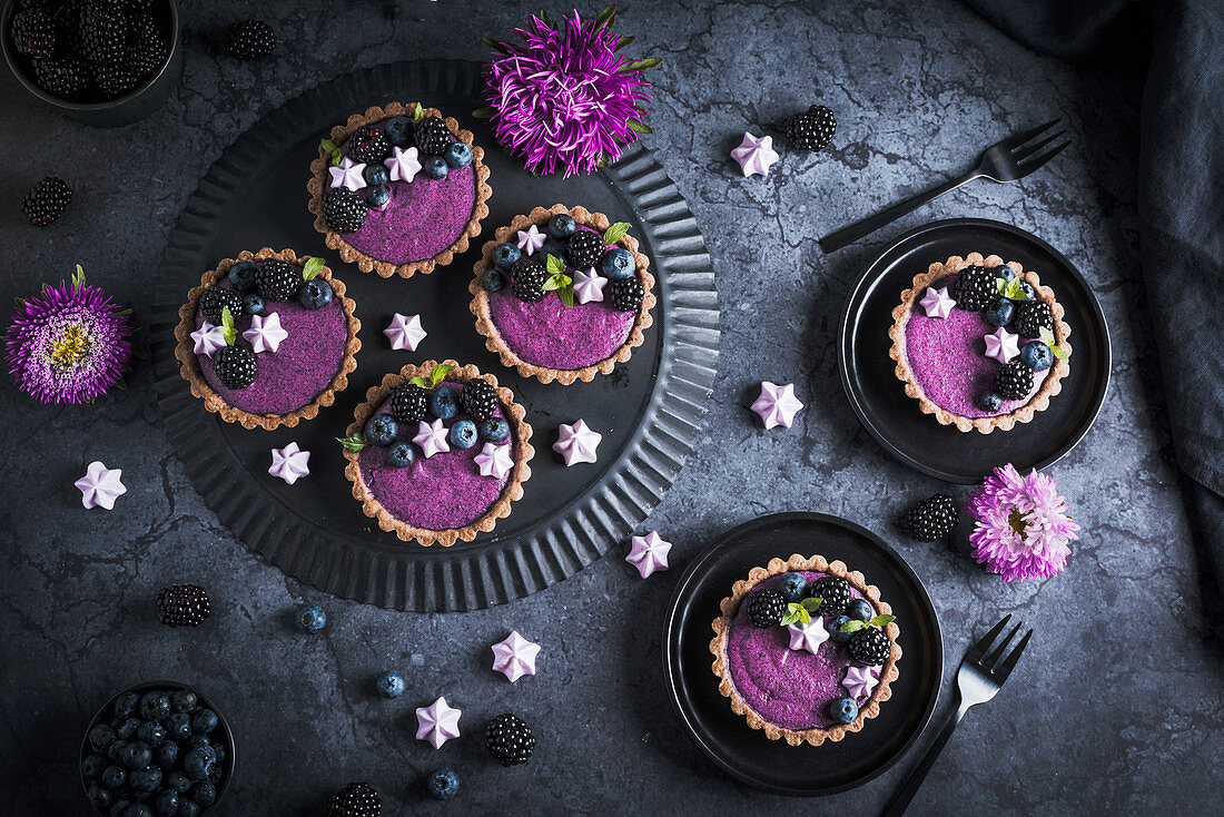 Blackberry yoghurt tartlets with mint leaves and meringue drops on black plates
