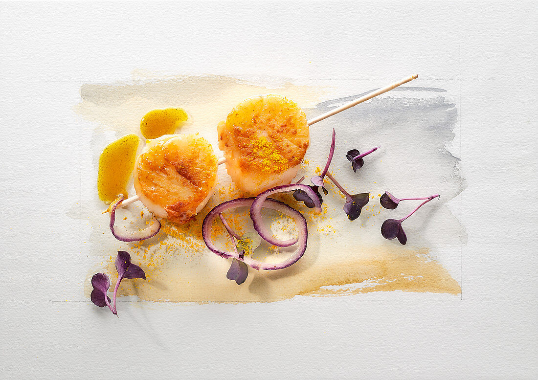 Food art: scallops on a stick, red onions, water cress and curry sauce on a page of watercolour