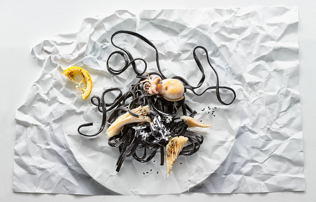 Food art: black linguine with octopus on creased paper