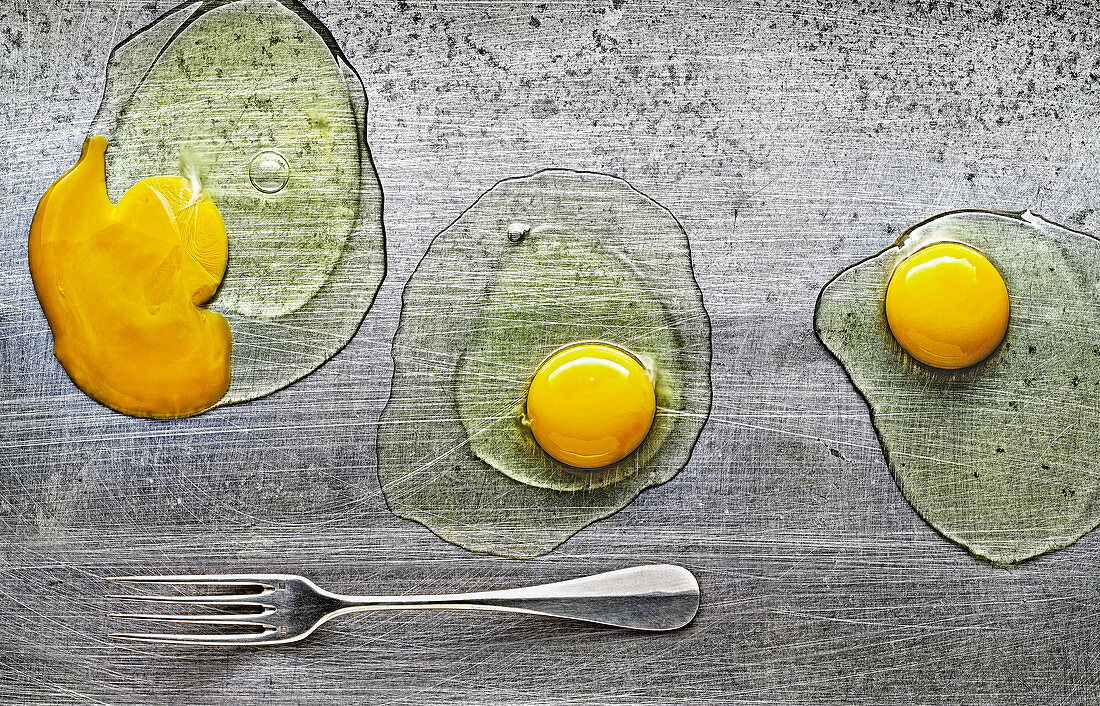 Food art: three cracked eggs on a metal surface