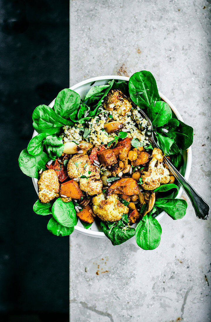 Grain bowl with roasted cauliflower, pumpkin, and chickpeas over lettuce