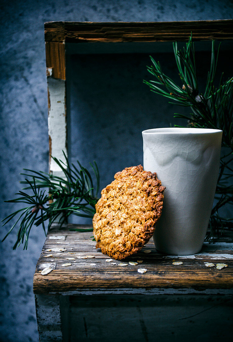 Thin honey and oat cookie with greenery and ceramic cup