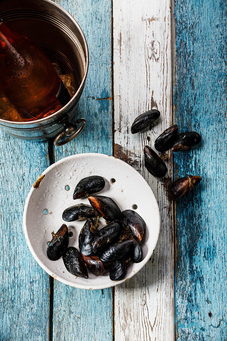 Raw Mussels Clams in vintage ceramic colander and Rose Wine in ice bucket on blue wooden background