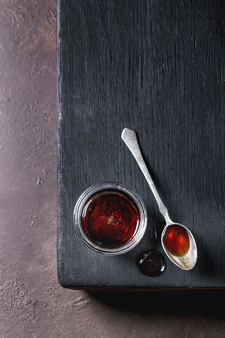 Homemade liquid transparent brown sugar caramel in glass jar standing on black wooden board