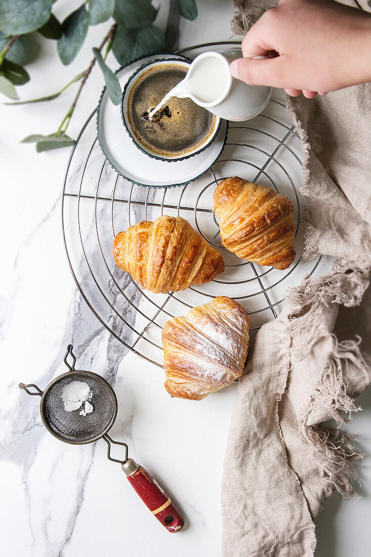 Croissants mit Puderzucker und einer Tasse Kaffee auf Abkühlgitter