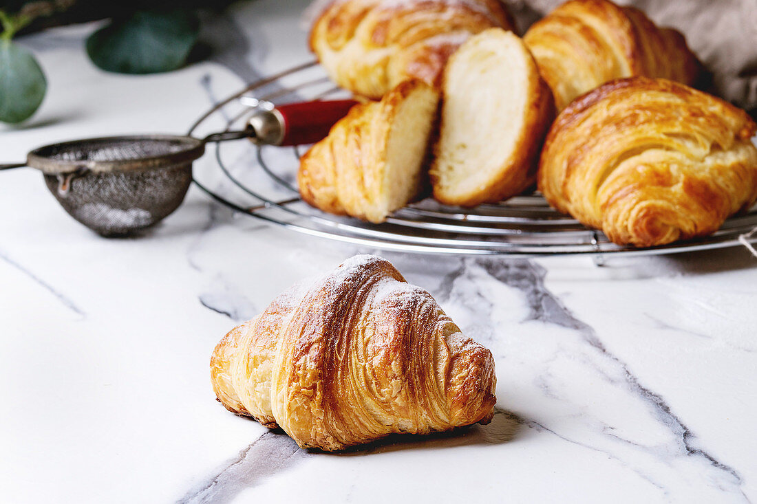 Croissants mit Puderzucker auf Marmortisch und Abkühlgitter