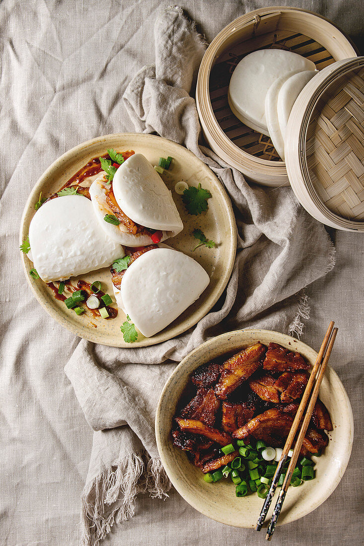Asian sandwich steamed gua bao buns with pork belly, greens and vegetables served in ceramic plate over linen tablecloth
