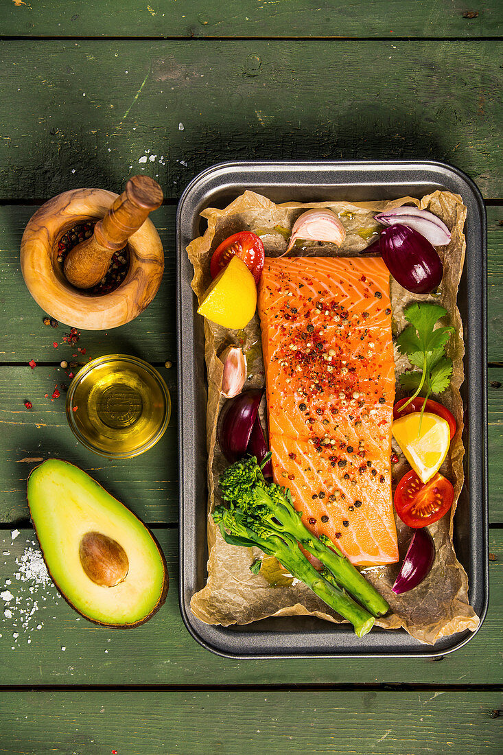 Baking dish with fresh raw salmon steak, vegetables and seasonings on green wooden background