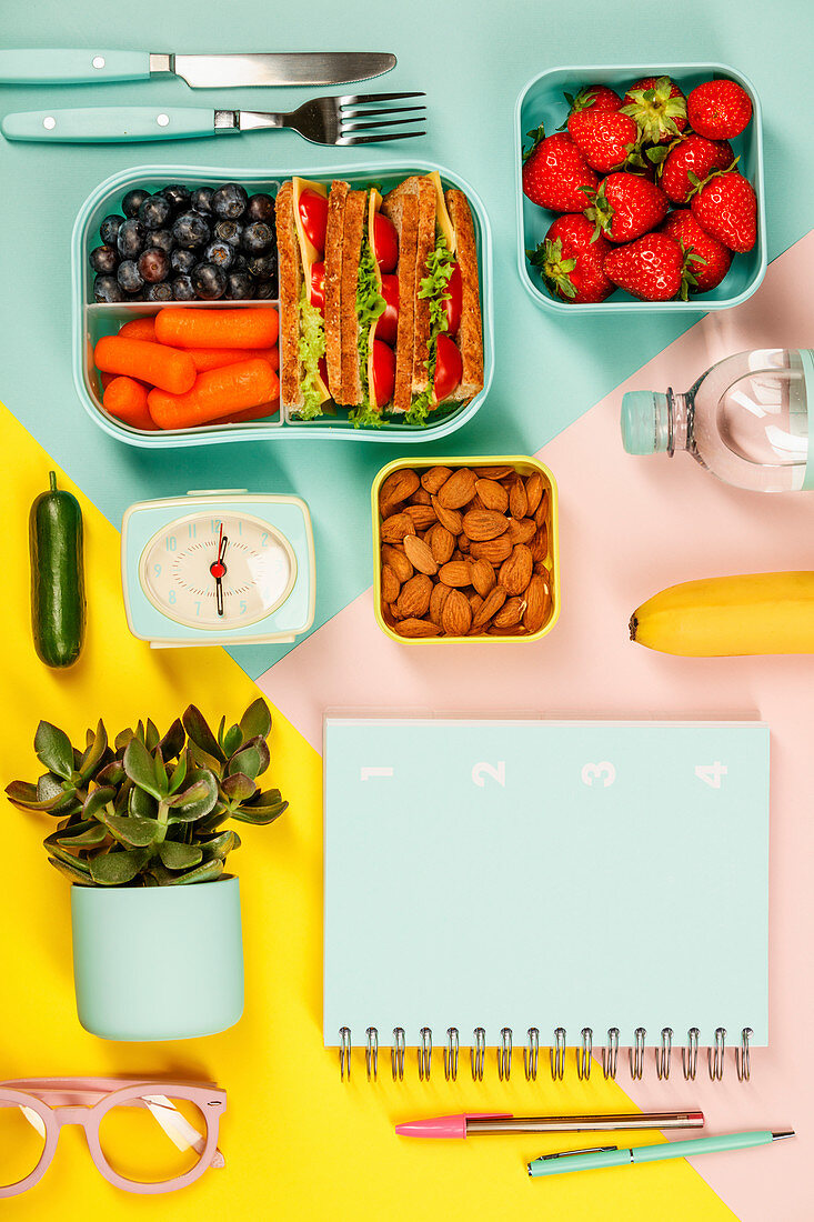 Creative flat lay with healthy lunch and office or school supplies on pastel colors background