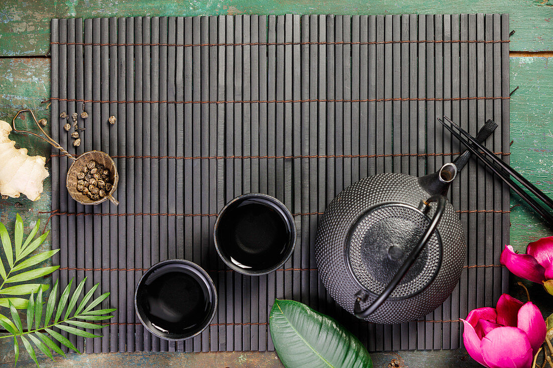 Stillleben mit asiatischer Teekanne und Teebechern auf Bambusmatte