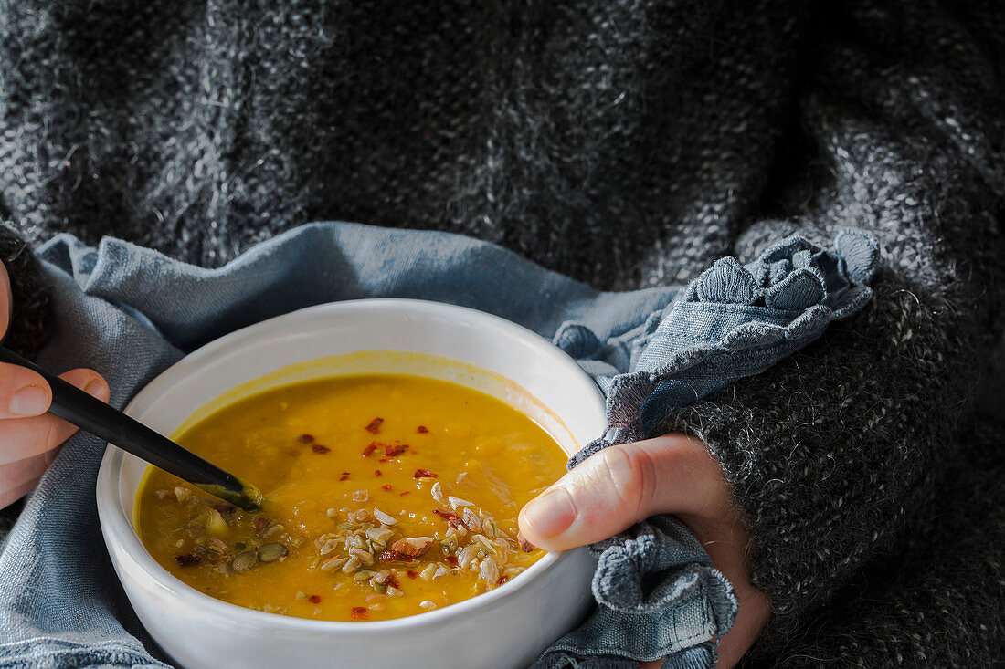 Hände halten Schälchen mit Kürbissuppe