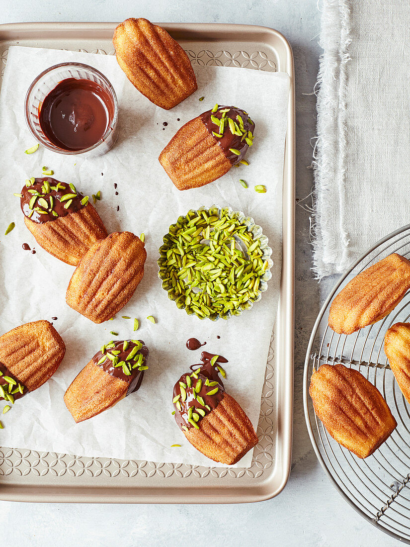 Madeleines mit Schokoladenglasur und Pistazien auf Backblech (Aufsicht)