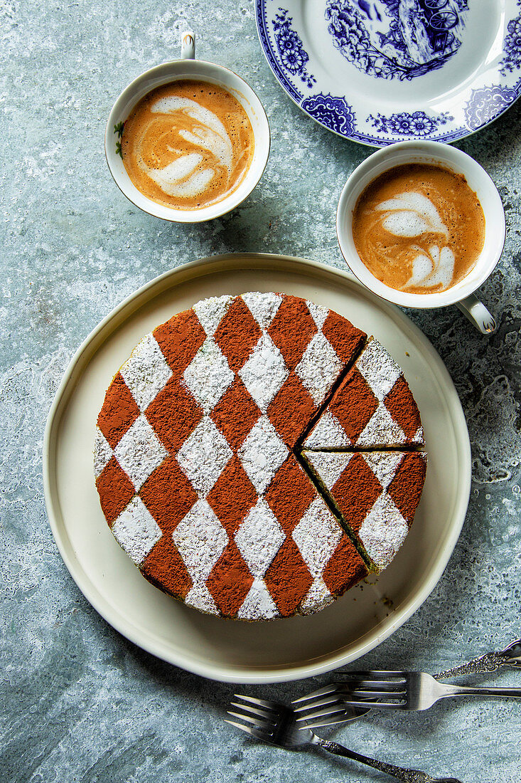 Sponge cake decorated with cocoa powder and icing sugar on a plate and two cups of coffee on the table