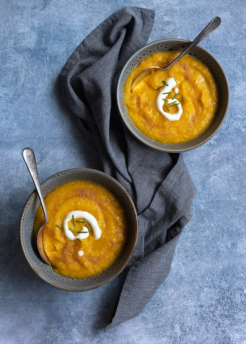 Two bowls of thick pumpkin soup with spoons on a blue textured background