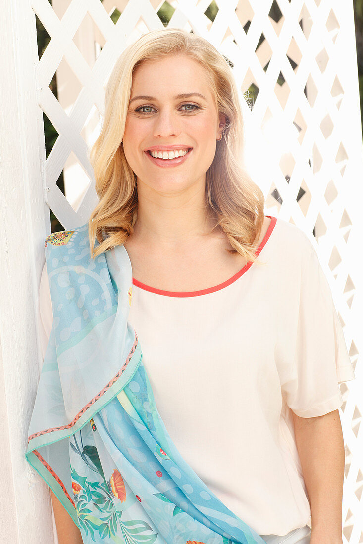 A blonde woman wearing a white t-shirt with red trim, and a summer scarf