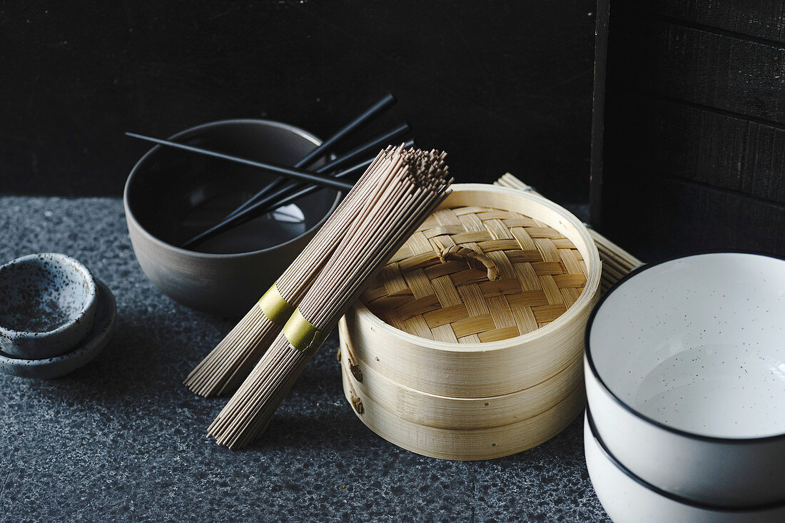 Soba noodles, bamboo steamer and asian cuisine props on dark background