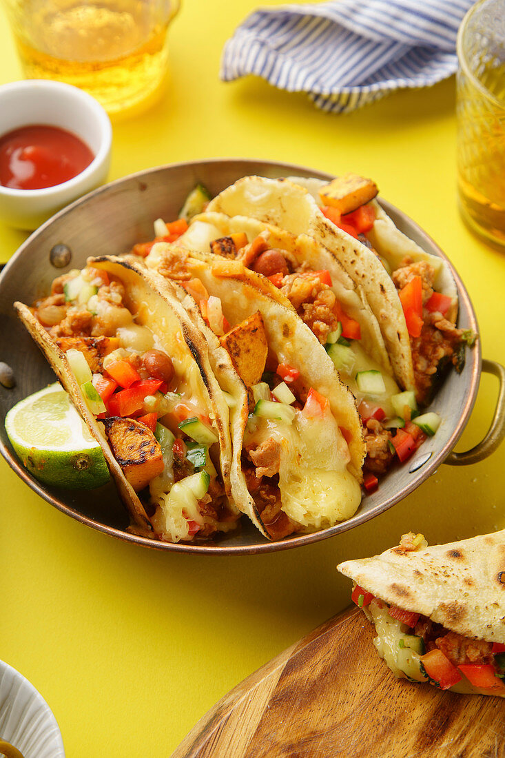 Close up of mexican tacos with chili con carnes and grated cheese served over a yellow background