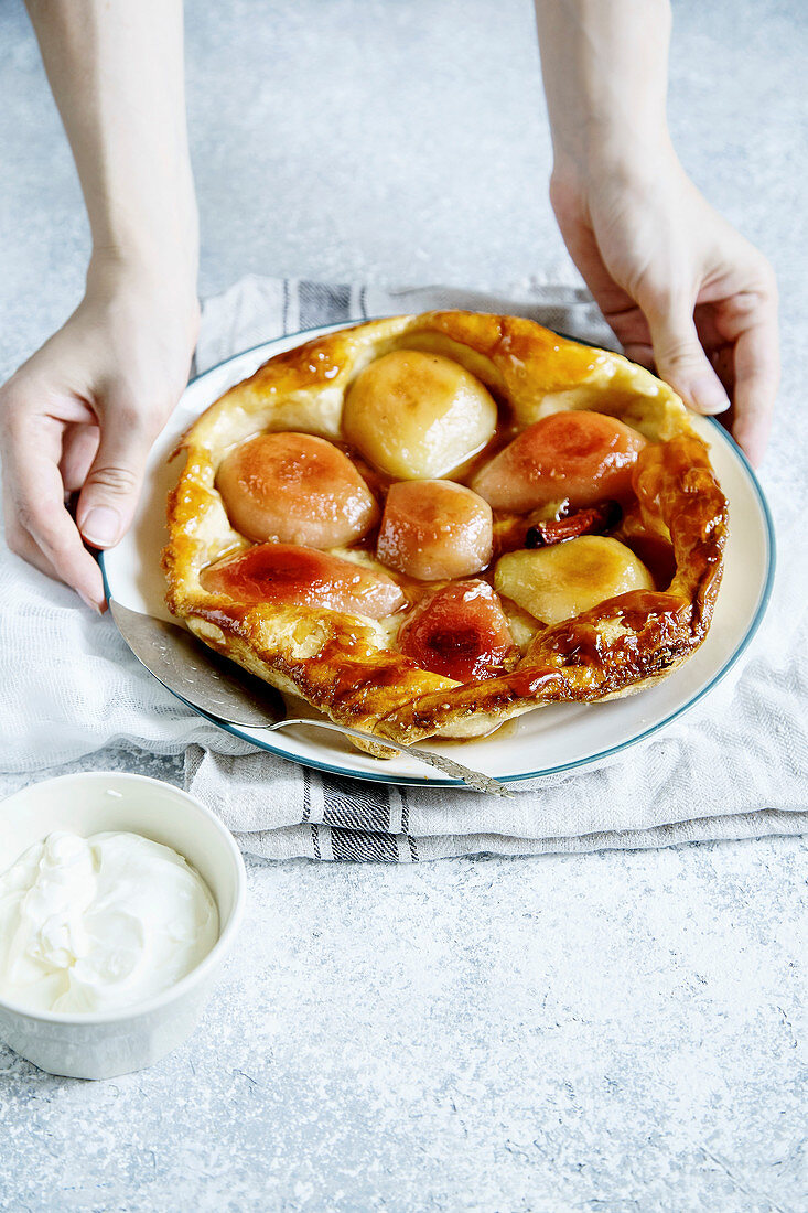 Female hands holding tart tatin with pears and whipped cream