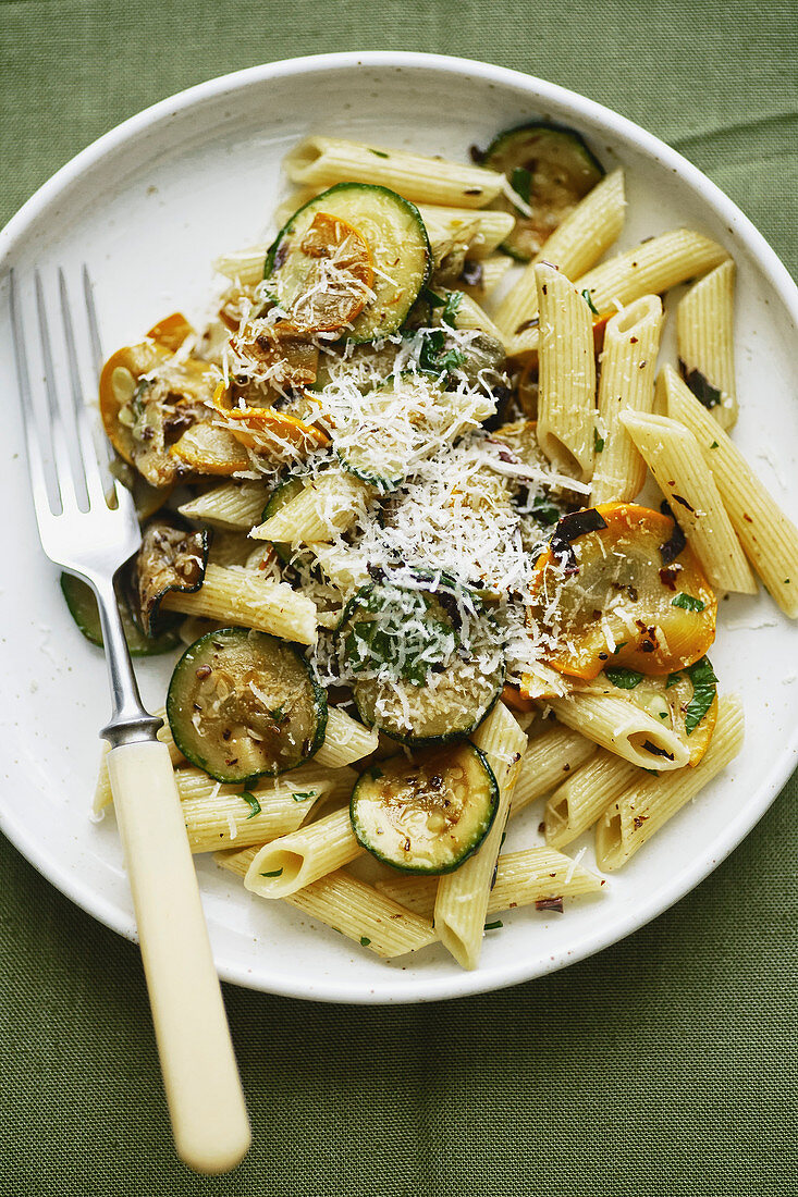 Overhead image of penne pasta with zucchini and summer squash on green rustic linen tablecloth