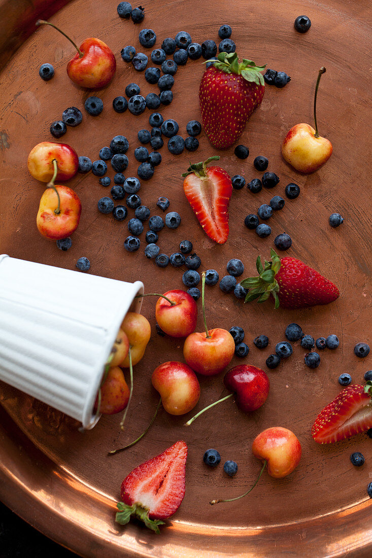 Rainier cherries, strawberries and wild blueberries on a copper tray and in a white tin cup