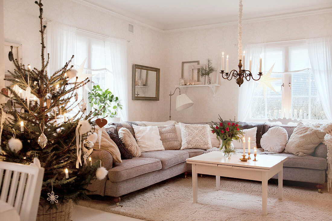 Geschmückter Weihnachtsbaum neben grauer Sofagarnitur im Wohnzimmer