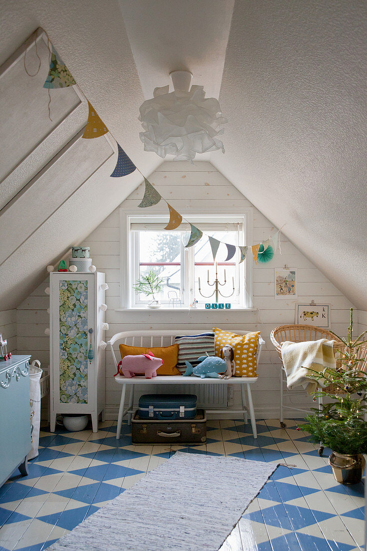 Cushions and soft toys on bench next to cabinet in attic room with blue-and-white chequered floor