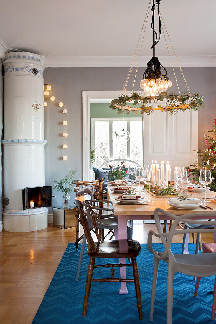 Wreath hung above table set for Christmas dinner in dining room with tiled stove