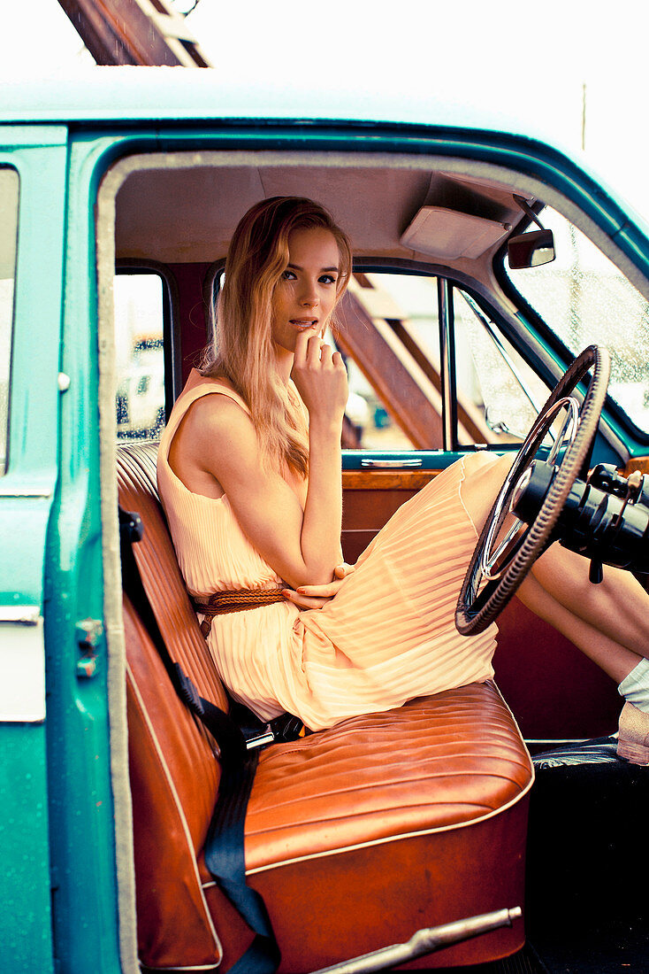 A young blonde woman wearing a yellow dress sitting in a car