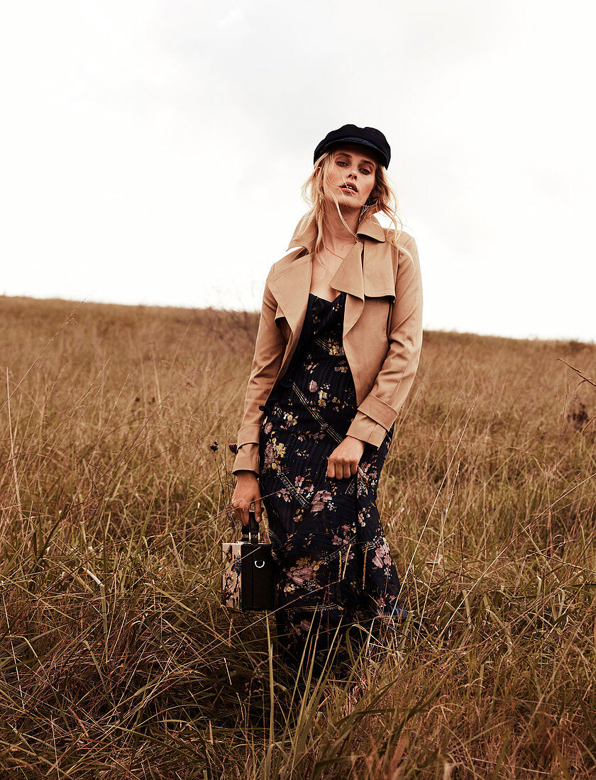 Blonde Frau mit Mütze im Kleid und brauner Jacke in der Natur