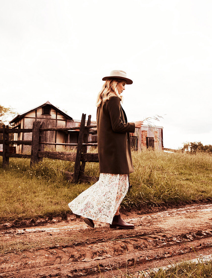 A blonde woman wearing wearing a hat, a light floral patterned dress and a brown coat