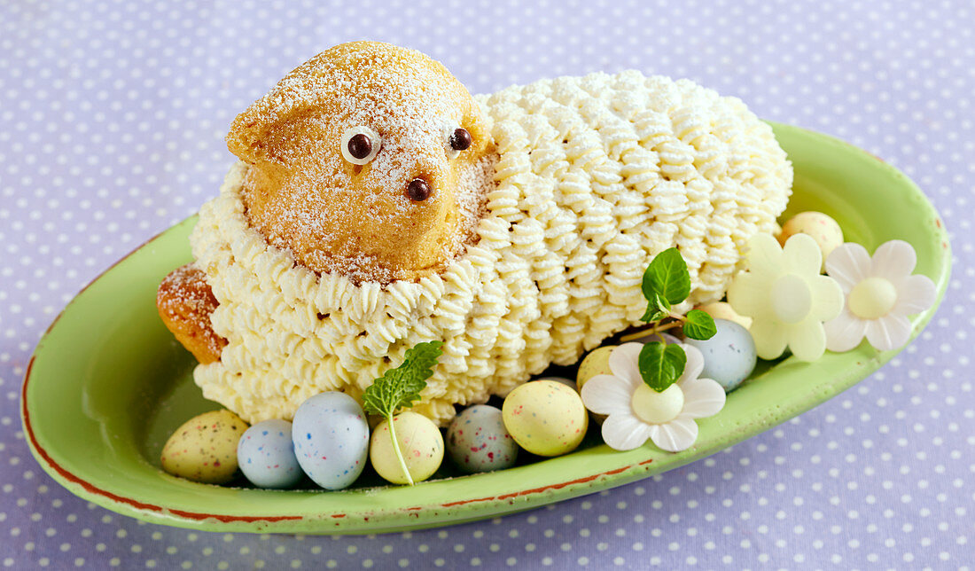 Baked Easter lamb bread with a buttercream coat, on an oval plate with sugar eggs