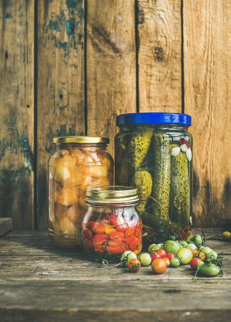Autumn seasonal pickled vegetables and fruit in glass jars, rustic wooden barn background