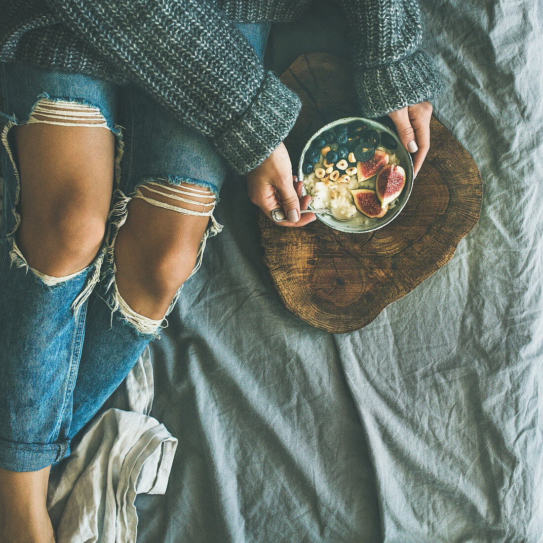 Woman in sweater and jeans eating rice coconut porridge with figs, berries, hazelnuts