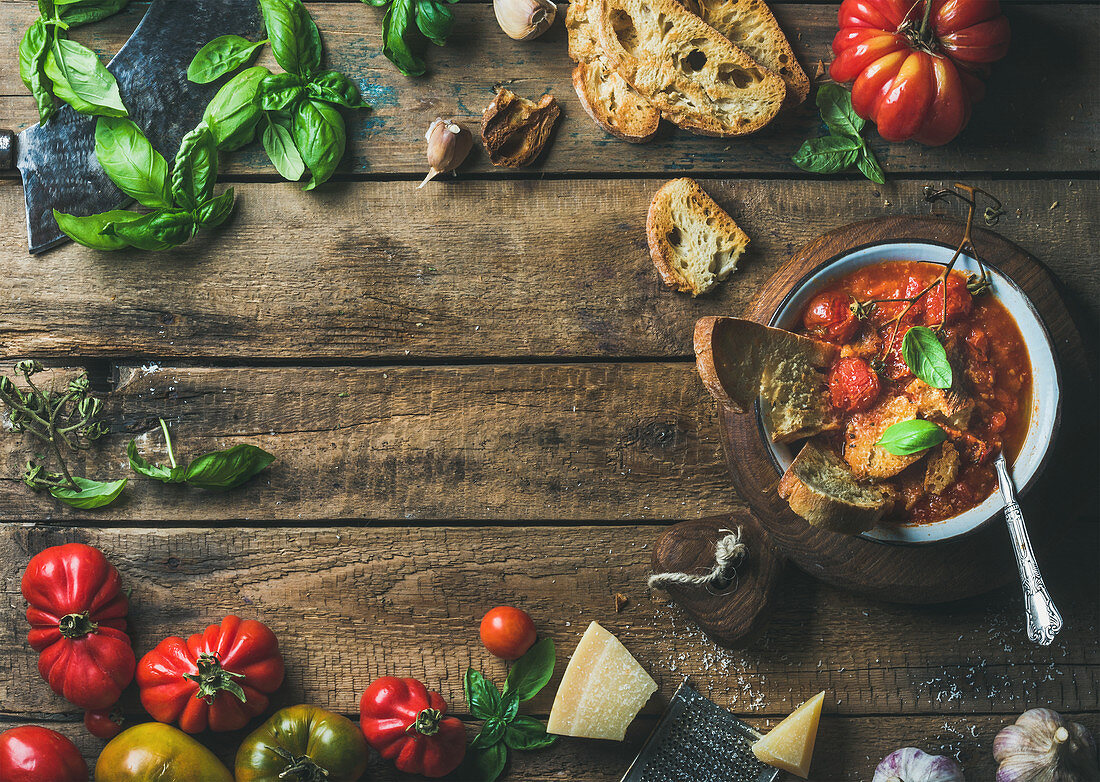 Tomaten-Knoblauch-Suppe auf Holzbrett mit Basilikum, Brot und Parmesan (Italien)
