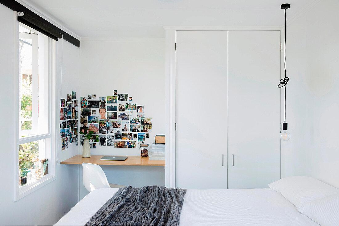 Double bed, pendant lamp, built-in wardrobe, small desk and photo gallery on the wall in a white bedroom
