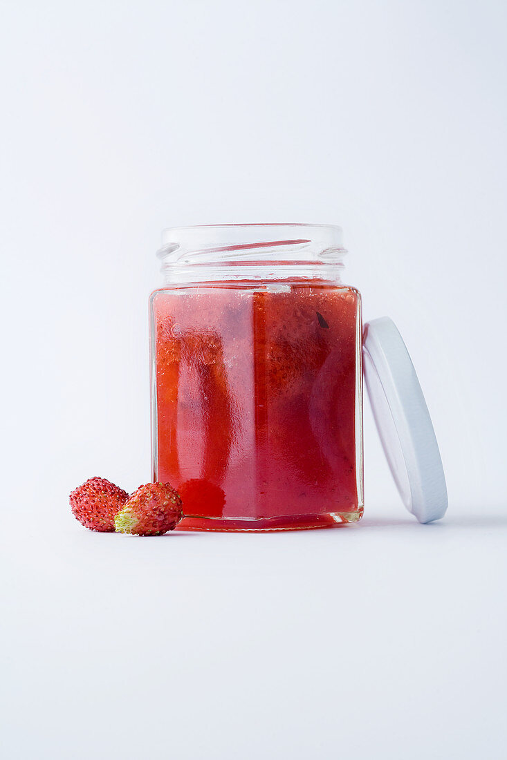 A glass of wild strawberry jam against a white background