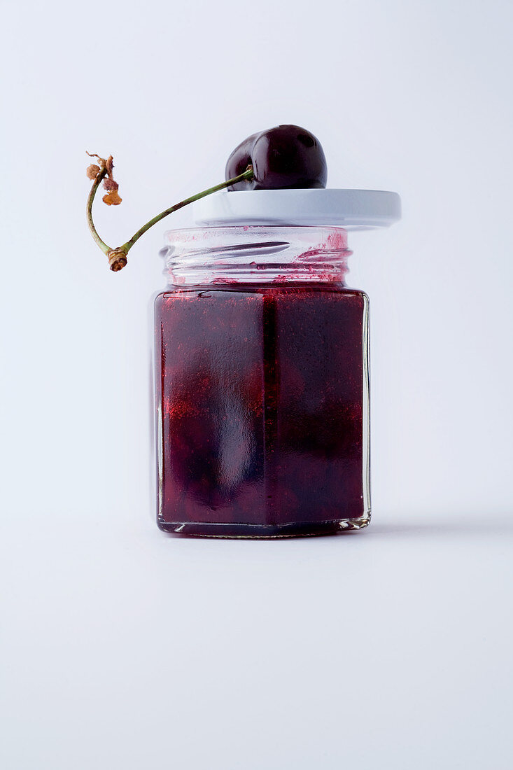 A jar of cherry jam against a white background