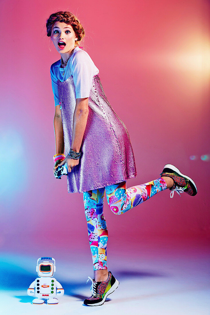 A girl with a plaited hairstyle wearing a glittery dress and colourful leggings playing with a toy robot
