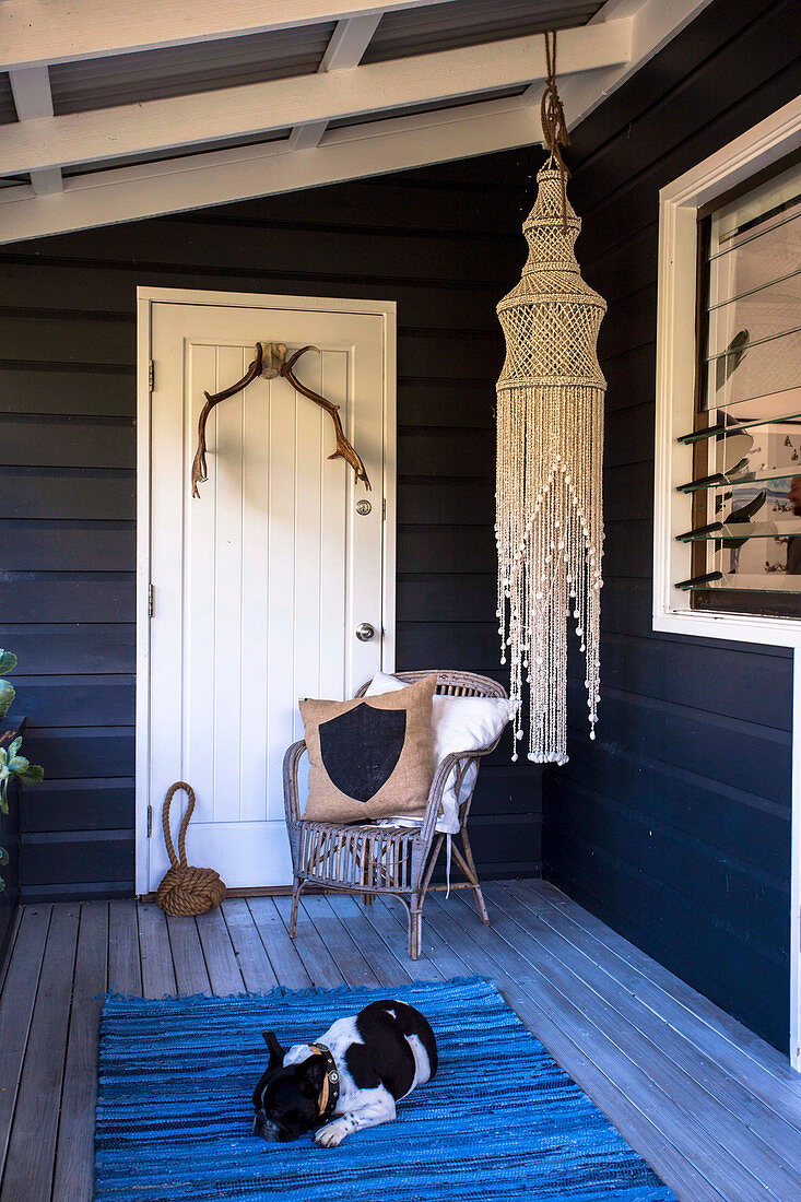 Chair in front of white door, macrame chandelier and dog on blue carpet on wooden veranda